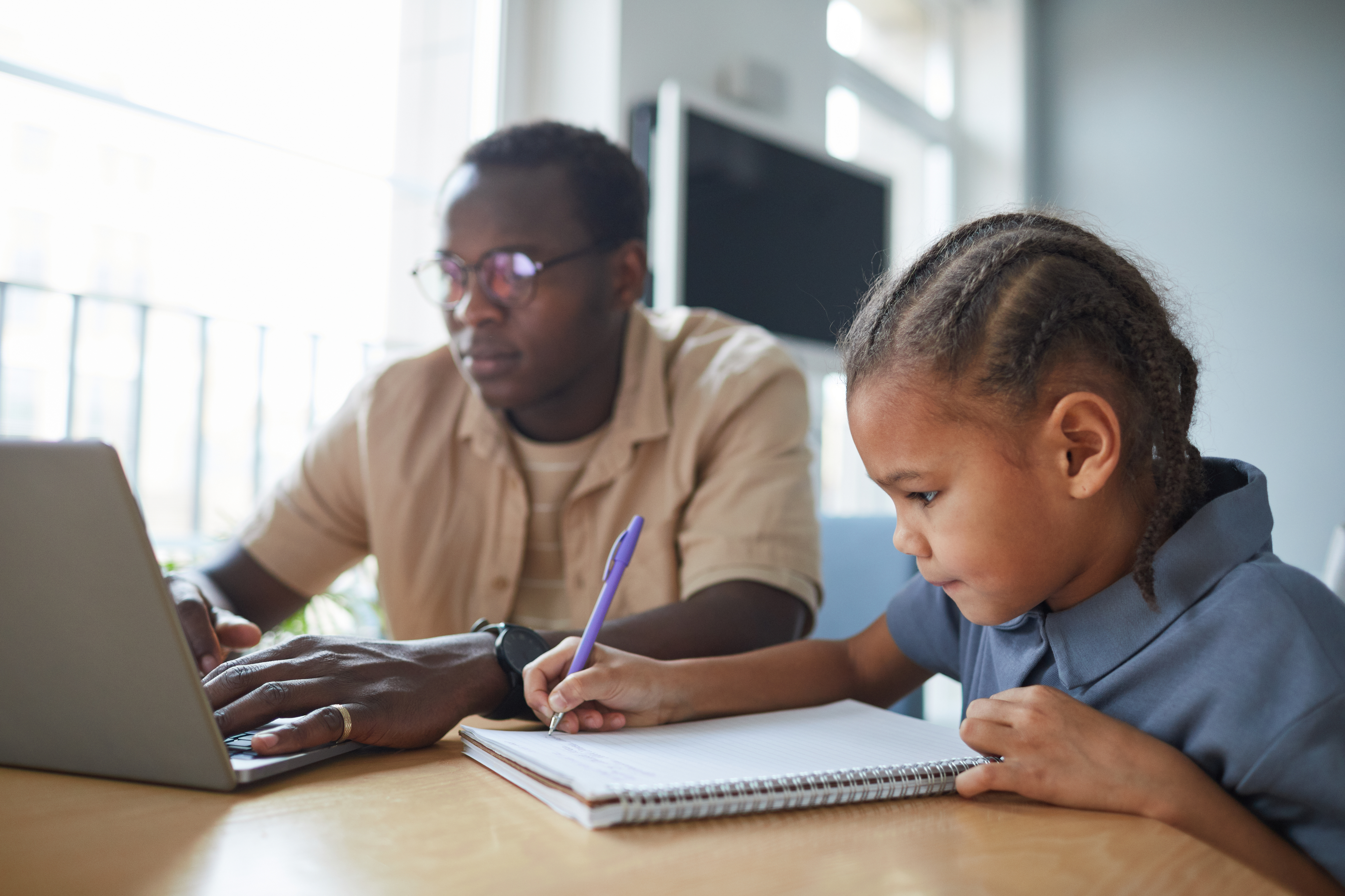 Child doing homework with adult on kitchen table