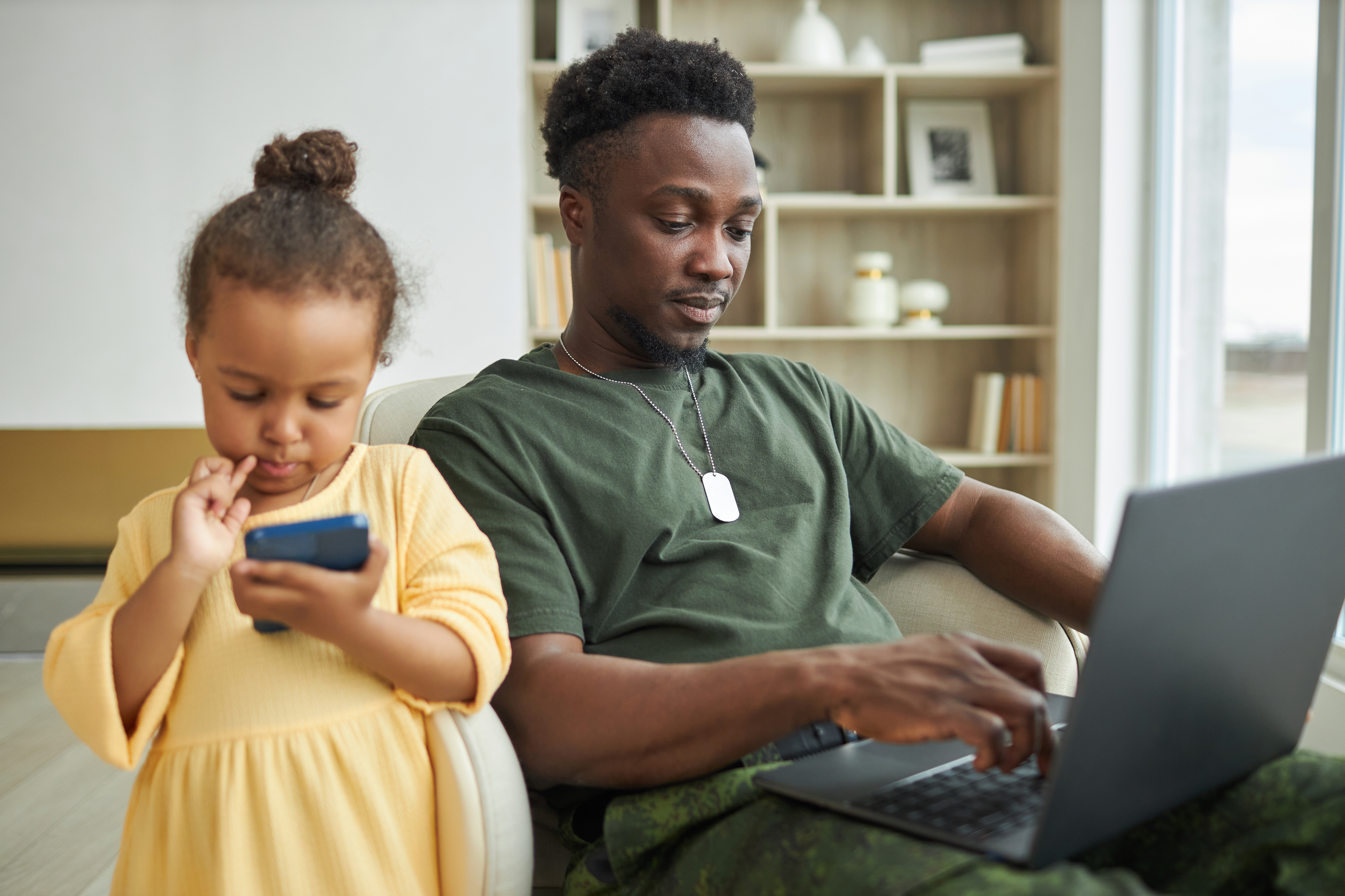 Child playing on mobile with dad on computer