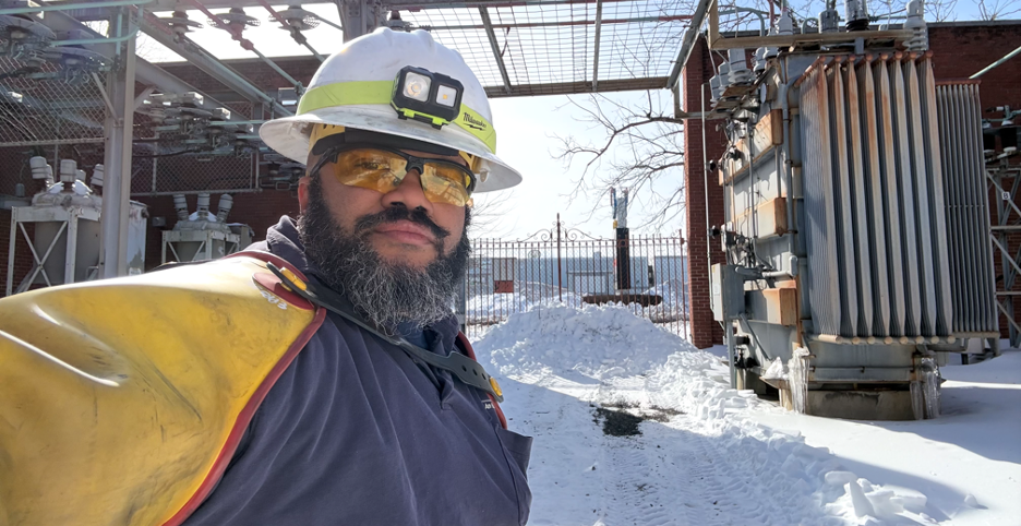 James Epps, a BGE service operator, stands beside a transformer in a snow-covered electrical substation while wearing protective gear.